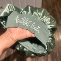 Green satin hair bonnet held by a hand with 'Briski Hair' branding.