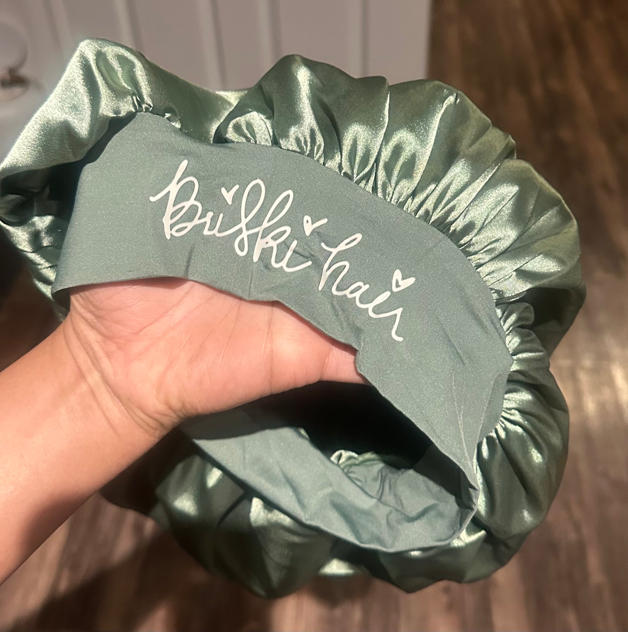 Green satin hair bonnet held by a hand with 'Briski Hair' branding.